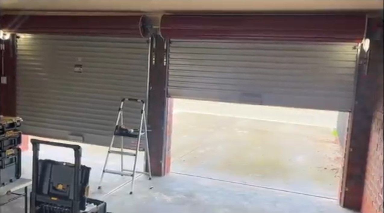 Two gray roller shutter garage doors, one open and one closed, with a ladder inside.